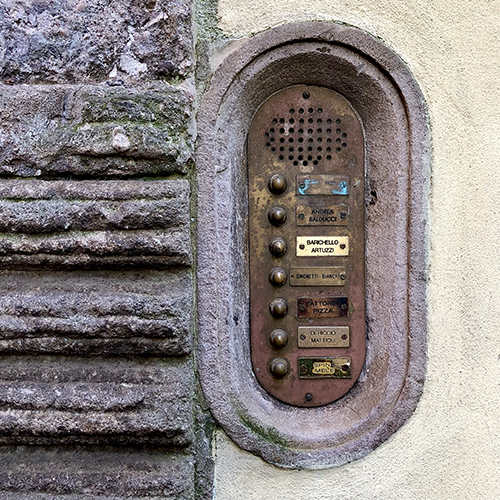 In the ancient walled city of Lucca, Italy, an image is captured of the ancient Roman invention of a door intercom, ha ha! (In a crusty old brass panel with quirky old buttons surrounded by carved stone are the delicious names: Balducci, Artuzzi, Bianchi, Mattioli, and Fattorini Pizza.)